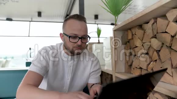 一个带眼镜的留着胡子的年轻人在露台上的笔记本电脑上工作视频的预览图