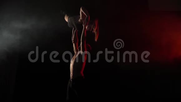 一个男人一手抱着一个女孩在黑暗中做杂技瑜伽慢动作视频的预览图