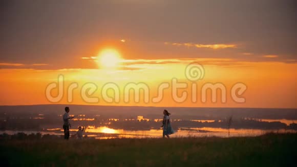 年轻女子和丈夫在球场上打羽毛球站在自己的小儿子旁边夕阳西下的夏日傍晚视频的预览图