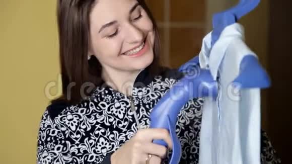 年轻女孩用蒸汽系统熨烫衣服蒸汽蓝色衬衫在家视频的预览图