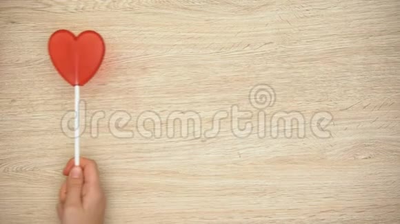 手拿心形棒棒糖在木制背景爱俯视视频的预览图