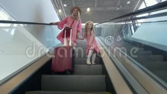 快乐的白种人母亲穿着夏装她的女儿在机场乘自动扶梯下楼梯视频的预览图