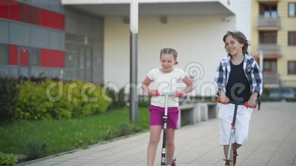 女孩和男孩骑着踢滑板车户外快乐可爱的孩子们在街头玩耍学习平衡踢脚板视频的预览图