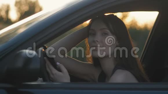 夕阳背景下年轻女性坐在车里用智能手机的画像视频的预览图