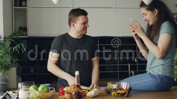 漂亮的年轻夫妇在家里的厨房里快乐地做饭和聊天为沙拉切菜的男人视频的预览图