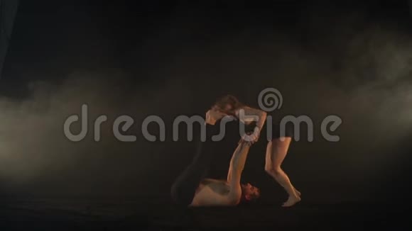 一个女人跳在一个男人的脚上做一个空翻在烟雾中做杂技瑜伽视频的预览图