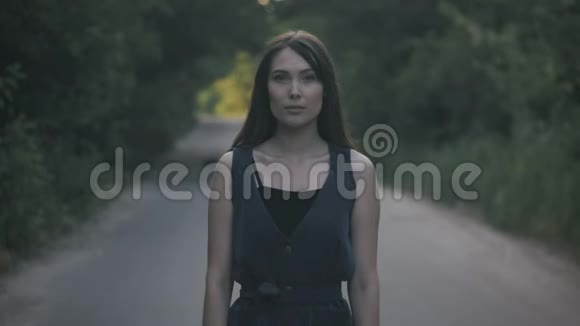 站在森林背景下道路上的年轻女子的肖像视频的预览图