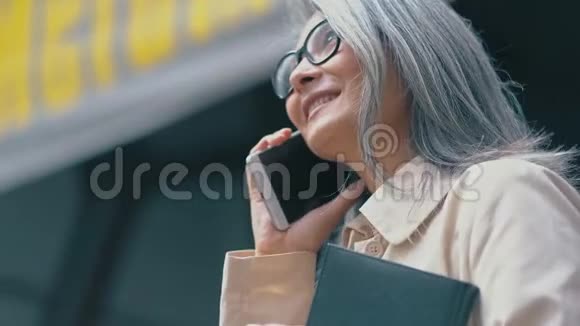 中年亚洲女人拿着笔记本在电话里说话视频的预览图