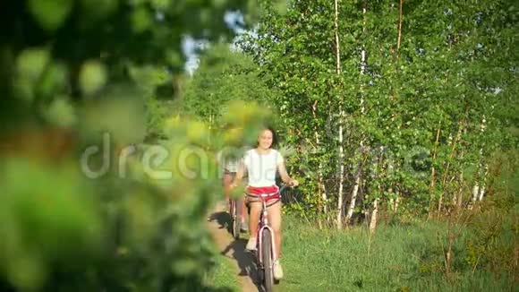 绿色的树枝女孩在自行车上欢笑和追赶绿色的树阳光明媚的夏日视频的预览图