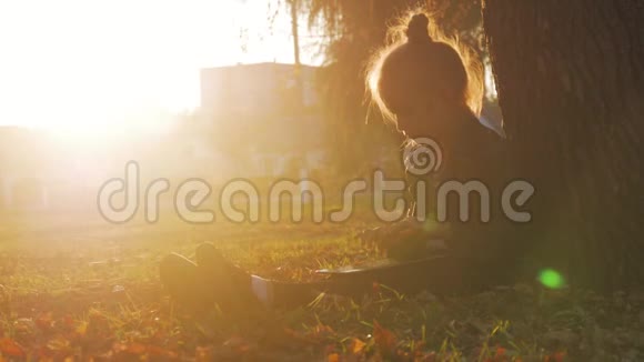 日落时分带着石碑的小女孩坐在秋天公园的一棵树下视频的预览图