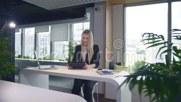 时尚的商务女性办公室里有平板电脑优雅的女士西装革履端着笔记本电脑和冲浪平板电脑坐在桌上视频的预览图