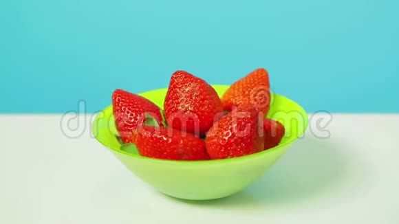 在蓝色背景下放在绿色碗里的红熟草莓以圆圈旋转视频的预览图