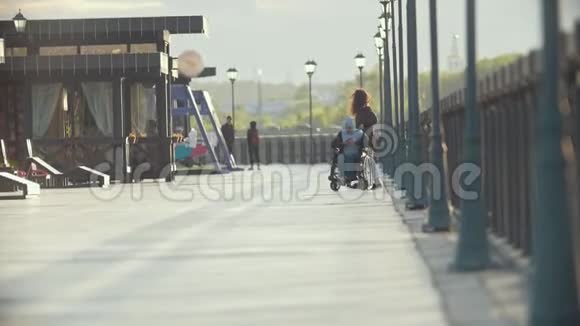 有残疾男子坐轮椅的年轻女子在码头上共度时光视频的预览图