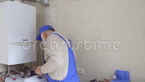 穿蓝色工作服的成年男子检查锅炉破裂的管道视频的预览图