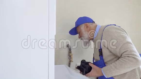戴着工作服的白发老人修理锅炉视频的预览图