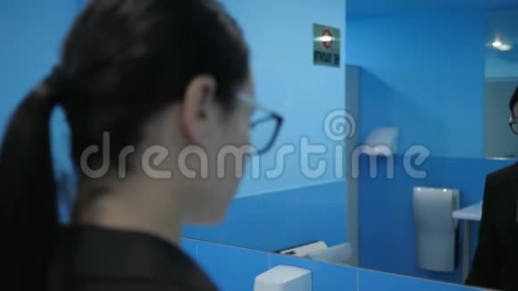 在公共浴室里一个被冒犯的女孩摘下眼镜对着镜子看自己视频的预览图