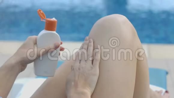 女士在她的腿上涂润肤露按摩动作在游泳池旁休息视频的预览图