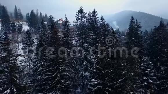 在冬季揭示山区有人居住地区的空中雪山山坡上的山村建筑视频的预览图