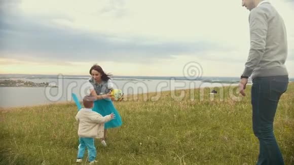 妈妈和一个小孩在玩球小孩跑向她球飞向爸爸阴天夏天视频的预览图