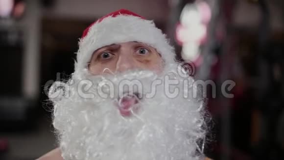 健身房里的圣诞老人正在做鬼脸展示二头肌视频的预览图