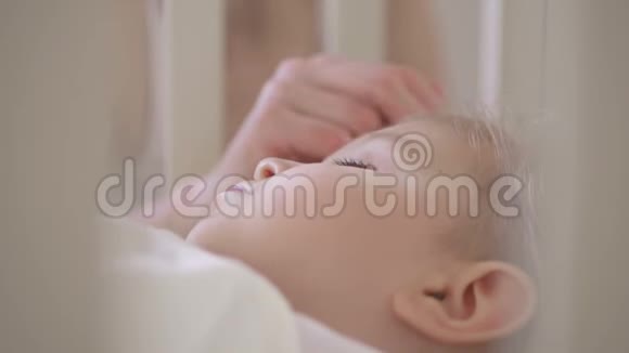 母亲抚摸一个熟睡的孩子的手产妇护理婴儿正在婴儿床上休息视频的预览图