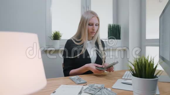 在办公室工作的女性数钱漂亮的金发女郎穿着商务西装在灯光下坐在办公室视频的预览图