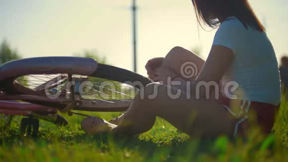 女孩坐在草地上滚动着自行车的轮子在后台骑着另一个女孩阳光明媚的一天视频的预览图