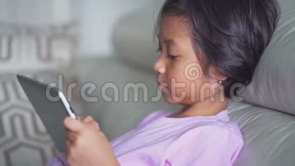 小女孩在沙发上用数码平板电脑视频的预览图