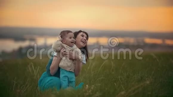 一个女孩坐在她旁边的绿草上是她的孩子他们在笑日落的夏日视频的预览图