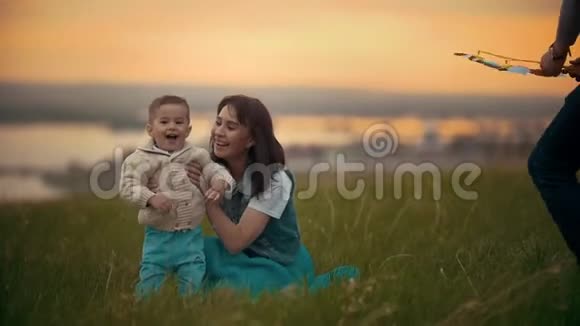 年轻的妈妈在草地上和宝宝玩孩子很开心夏天的傍晚日落视频的预览图