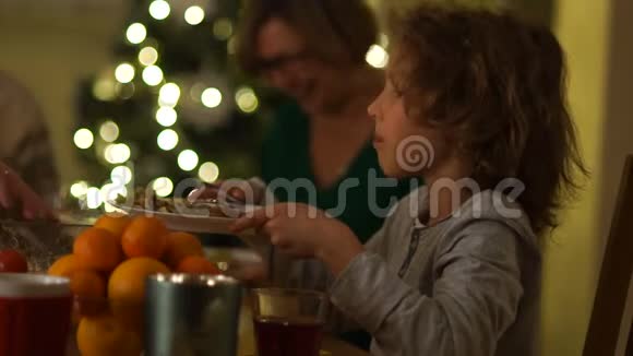 在一棵新年树的背景下一个小学生和他的祖父母在圣诞桌上男孩伸出盘子视频的预览图