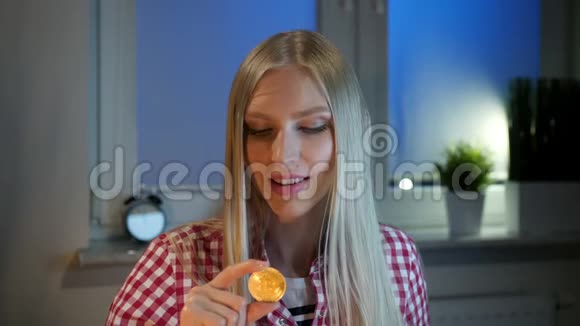 幸福的女人拿着比特币竖起大拇指年轻的金发女郎穿着便装坐在黑暗的窗户上视频的预览图