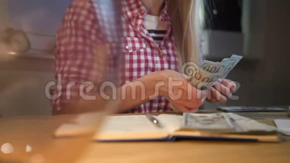 在工作台数现金的女人漂亮的金发女郎穿着格子衬衫晚上坐在房间里穿着木制的视频的预览图