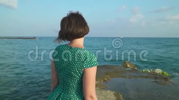 穿着礼服的女人在海浪中在海岩上行走慢动作视频的预览图