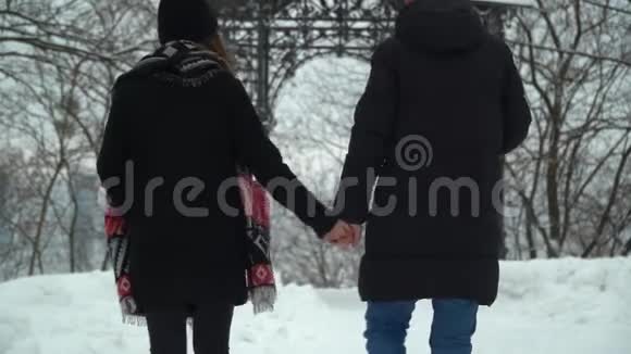 年轻的男人和女人在冬天的公园里散步白雪覆盖着双手冬闲的幸福恩爱夫妻回去视频的预览图