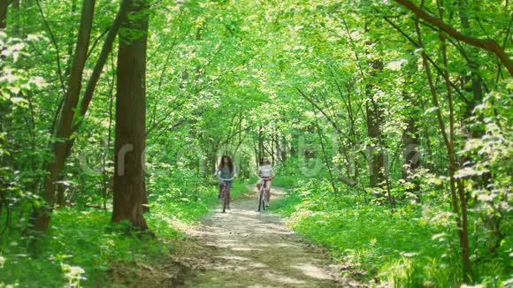 阳光明媚的一天在森林里两个女孩骑着自行车在小路上交流视频的预览图