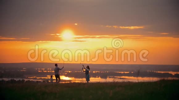 女孩和男孩在球场上打羽毛球站在他们的小儿子旁边夕阳西下的夏日傍晚视频的预览图
