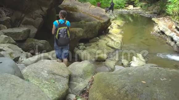 骑自行车的美女背着背包用智能手机在山河上拍照丛林中有巨石和绿苔视频的预览图