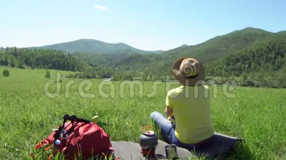 那个拿着旅游棒和红色背包的旅行者女人坐在草地上煤气炉上的茶壶站着视频的预览图