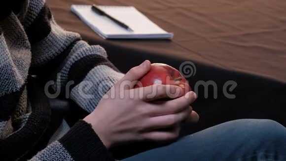 一个穿灰色毛衣的年轻人的手这家伙正在考虑一个成熟的红苹果学生艺术家或作家注视频的预览图