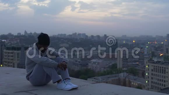 一个忧郁的人坐在摩天大楼的边缘思考着生活黄昏的薄雾视频的预览图
