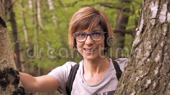 森林里户外的成年妇女肖像微笑着看着相机戴着绿色眼镜表情开朗h视频的预览图