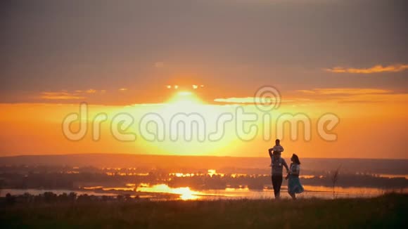 一家人迎着夏日的夕阳散步爸爸妈妈牵着手儿子坐在肩上视频的预览图