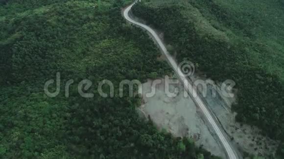透过茂密的绿色植物和茂密的热带雨林山地景观的乡村道路鸟瞰视频的预览图