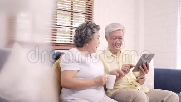 亚洲老年夫妇在家里的客厅里使用平板电脑和喝咖啡视频的预览图
