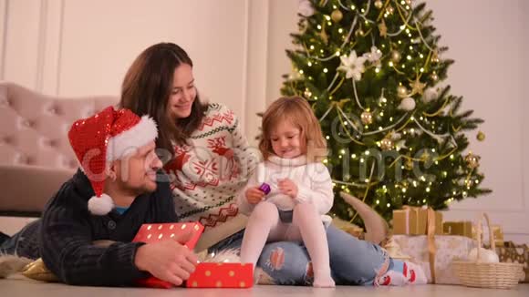 圣诞老人家躺在地板上父母和婴儿在卧室有乐趣人们在家放松冬季视频的预览图
