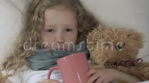抱着玩具熊躺在床上抱着杯子看着摄像机哭着生病的女孩视频的预览图