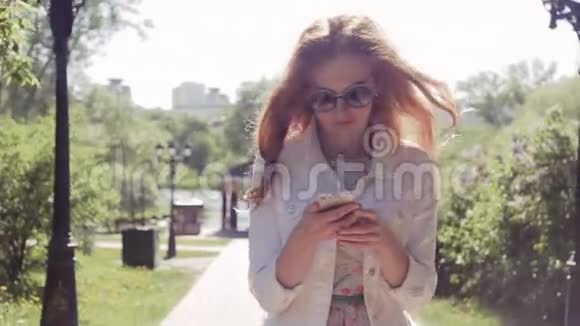 年轻的红发女子带着电话在公园散步动作缓慢视频的预览图