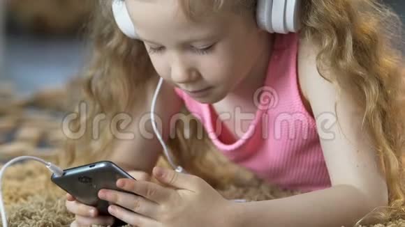 小女孩躺在地毯上用手机听耳机听音乐视频的预览图