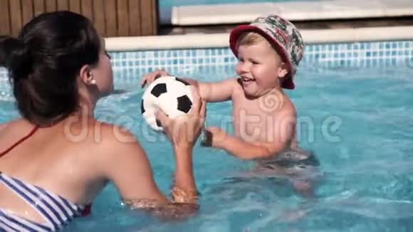一个快乐的孩子和他的母亲在游泳池里玩耍试图去踢足球视频的预览图